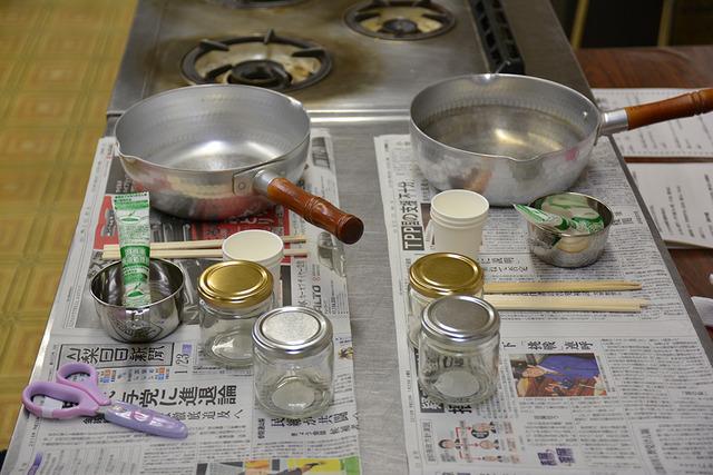 新聞紙の上に片手鍋、廃油処理剤、空き瓶等の材料が並べられている写真