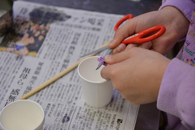 子どもが紙コップの上でクレヨンをはさみで削っている写真