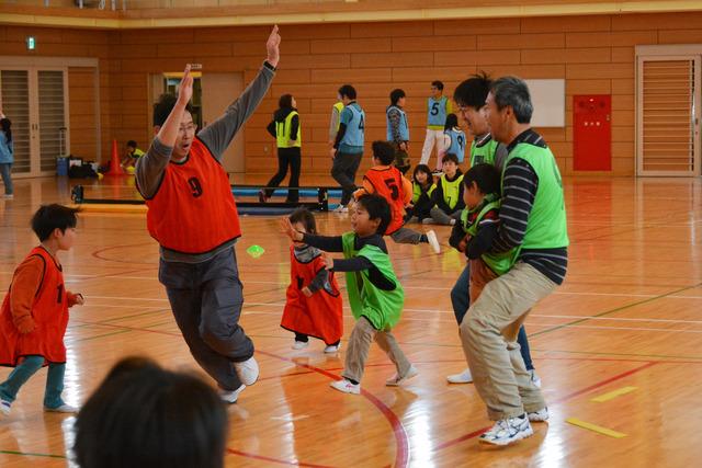 緑と赤のユニフォームを着た子どもと大人が走っている写真