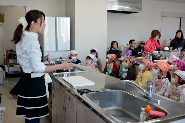 エプロン、三角巾、マスクを着用した子どもたちが講師の荒井先生の話を聞いている写真