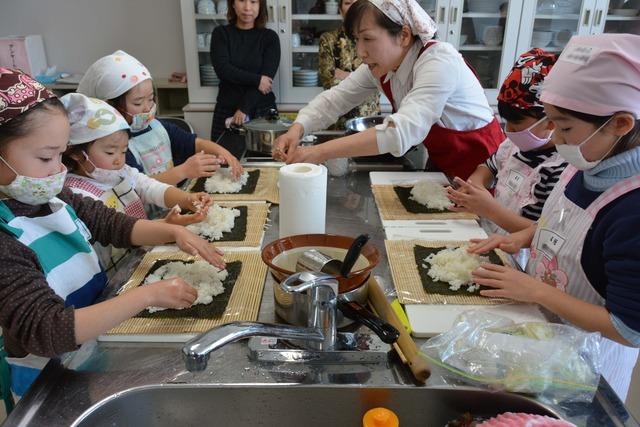 先生に教えてもらいながら5人の子どもたちが巻きすの上に海苔を酢飯を乗せている写真