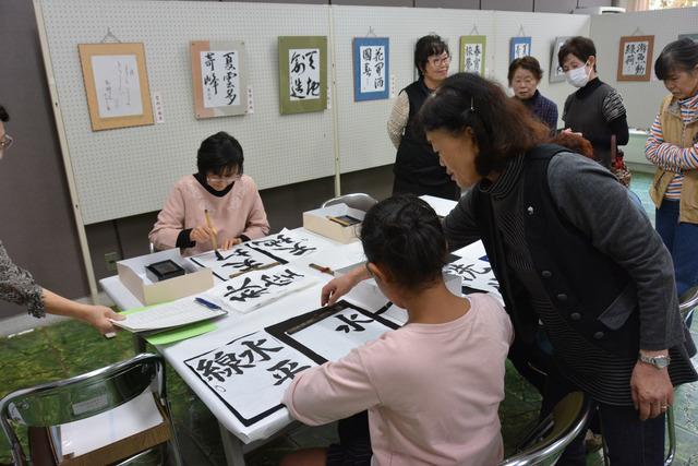 指導を受けながら、習字をする参加者の写真