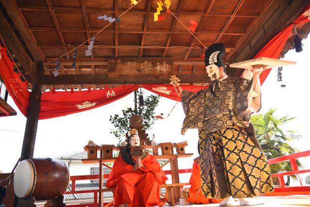 衣装を着て、面をつけて、神楽が行われている写真