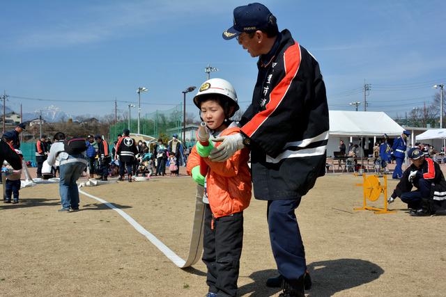 子ども用の消防服を着てホースを構える男の子の写真
