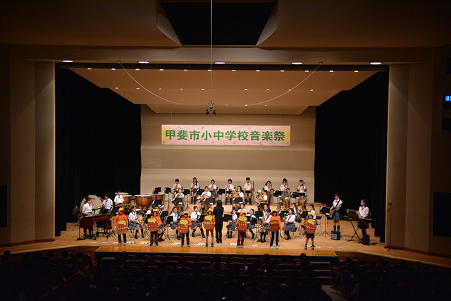 前一列がオレンジ色の衣装を着て演奏する竜王北小学校吹奏楽部の写真
