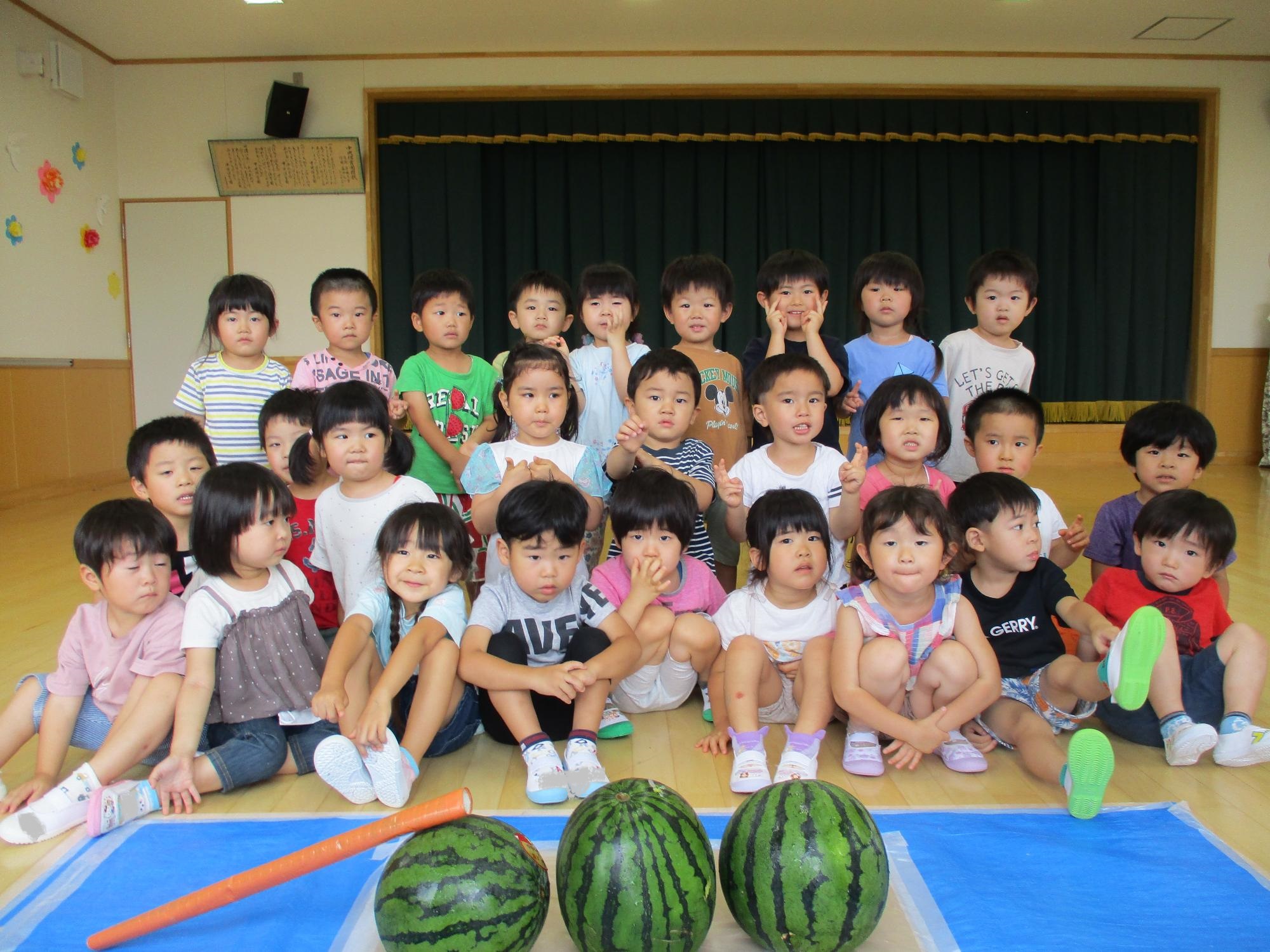 スイカと一緒に写真を撮るすみれ組の子ども達です。