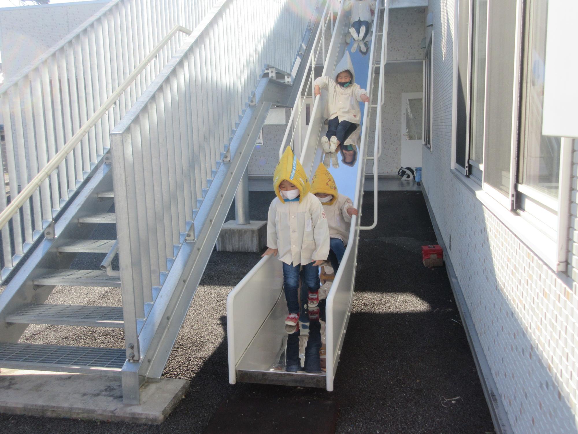 避難訓練で避難用のすべりだ台を初めて使用して避難している写真です。