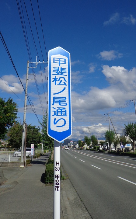 「甲斐松ノ尾通り」と縦書きしてある道路案内標識の写真