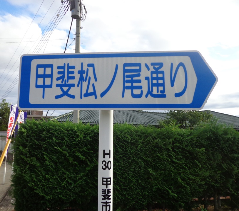 「甲斐松ノ尾通り」と横書きしてある道路案内標識の写真