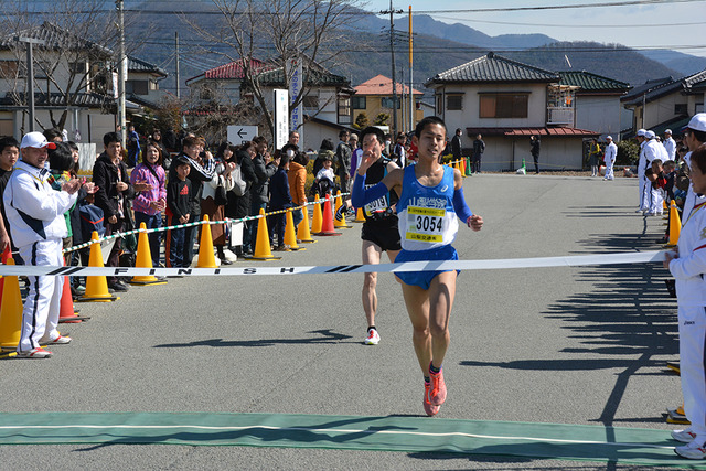 (写真)手を挙げゴールテープを切るランナー