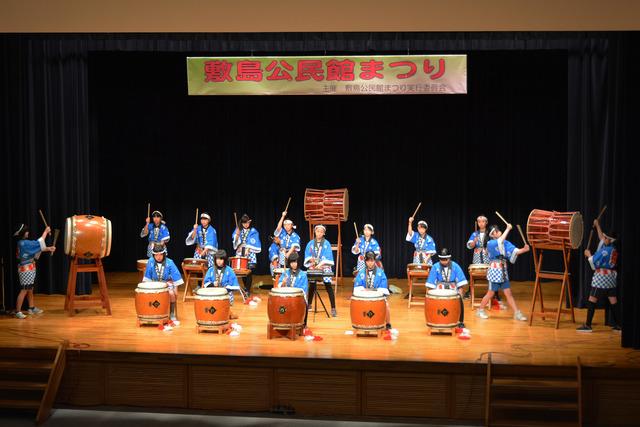 青い法被を着た小学生たちが和太鼓を叩いている写真