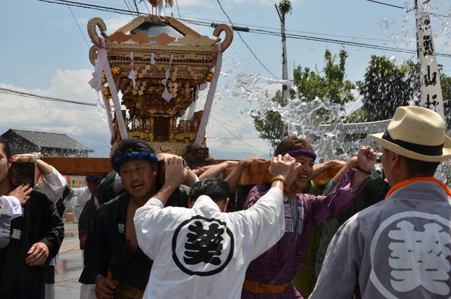 神輿を担ぐ男性達に水がかけられている写真