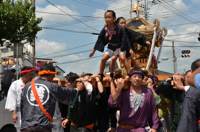 大人が担ぐ神輿の上に立っている子ども達の写真