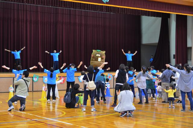 舞台の上に「やはたいぬ」が立ち、先生と参加者がラジオ体操をしている写真