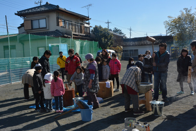 屋外で杵と臼で餅をつく人々の写真