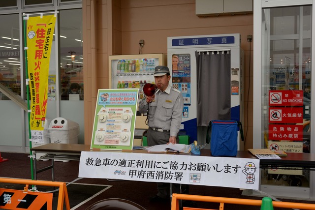 救急車の適正利用にご協力お願いしますと書かれた看板とスピーカーで話す男性の写真