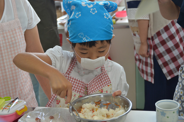 ボールに入った五目いなりのご飯をスプーンでまぜる女の子の写真