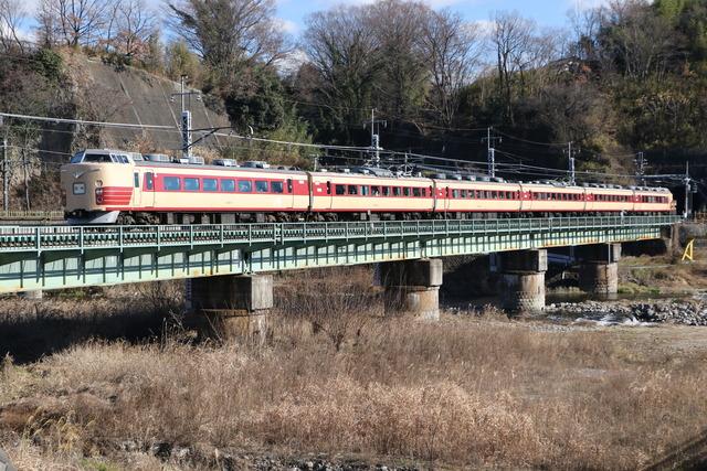 クリーム色に赤いラインが入った「あずさ50周年記念列車」が橋の上を通過している写真
