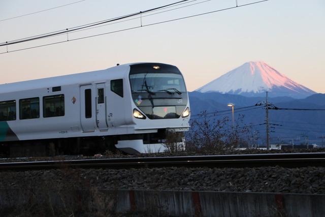 夕暮れの富士山を背景に走行する白い車体の「E572系あずさ号」の写真