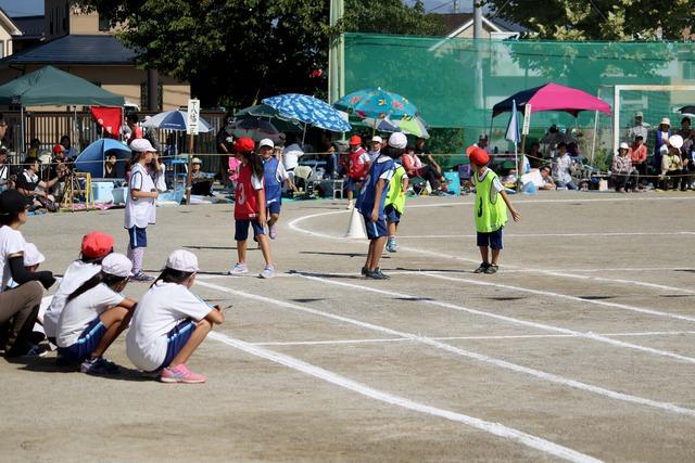 校庭のトラックでリレーのバトンがまわってくるのを待つ児童の写真