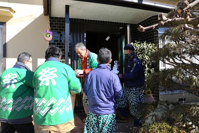 緑の法被を着た男性が区内の住民を家を訪ねている写真