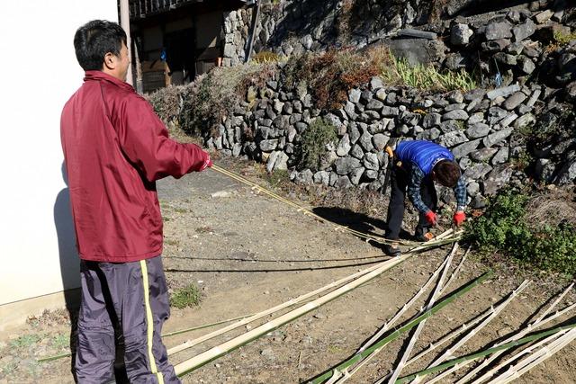 なたを使って竹を割り、節取りをする男性たちの写真