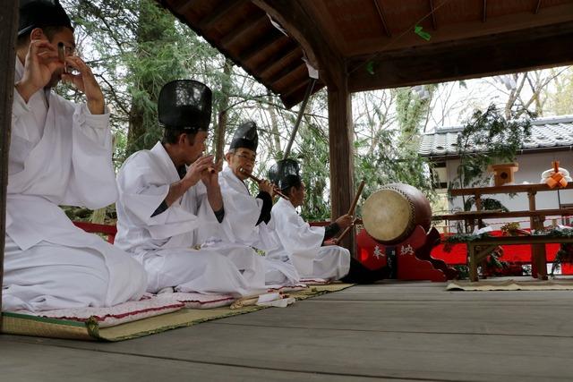 白い衣装を着た男性4人が座って太鼓や横笛を演奏している写真