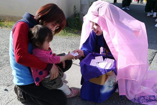 姫が小さな子供を連れた親子に福銭を配っている写真