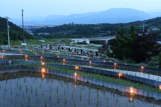 暗くなってきた棚田に火のついたろうそくが並んでいる写真