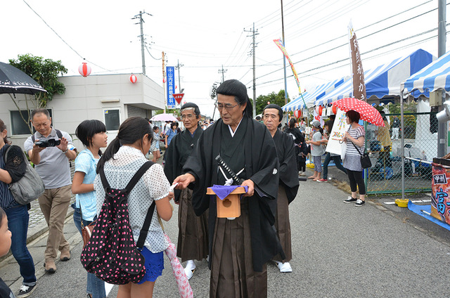 (写真)山県大弐仮装行列が来場者にお守りを配る様子