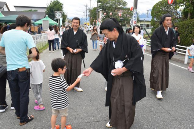 (写真)大弐仮装行列がお守りを配る様子