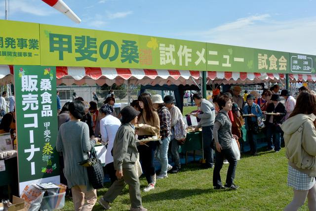 「甲斐の桑試作メニュー試食会」と書かれたブースに沢山の人が集まっている写真