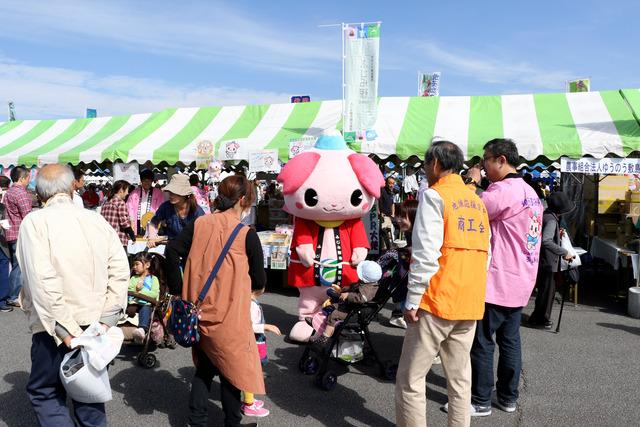 ピンクの桜の花びらの耳を付け頭に富士山を乗せた埼玉県ふじみ野市のゆるキャラ「ふじみん」の周りに沢山の人が集まっている写真