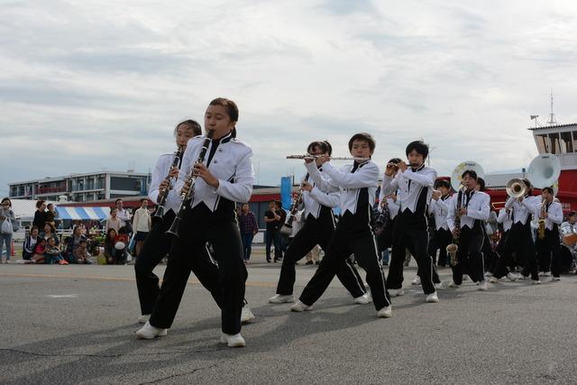 竜王北中学校の白と黒の衣装を着た学生が楽器を演奏してマーチングしている写真