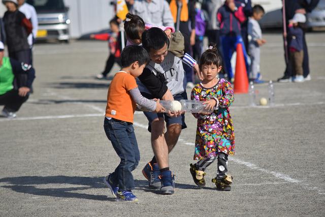 竜王新町大運動会のカンカン・ボールの種目で左右のペットボトルでソフトボールを挟んで運んでいる親子の写真