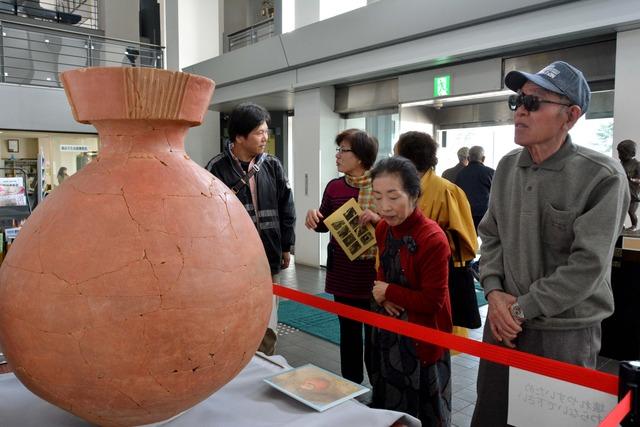 来場者の男女がロビーに展示された「大型赤彩壷」を見ている写真