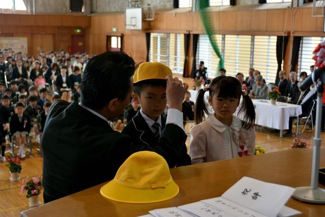 黄色い帽子を贈られる新入学児童代表の男の子と女の子の写真