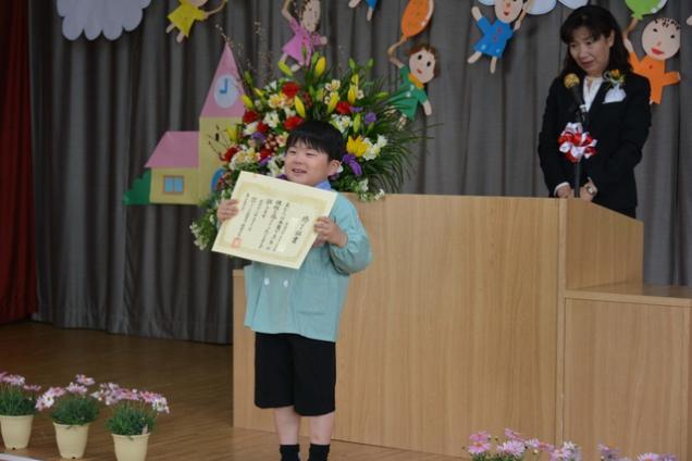 舞台の上で卒園証書を手に持ち笑顔で立っている園児の写真