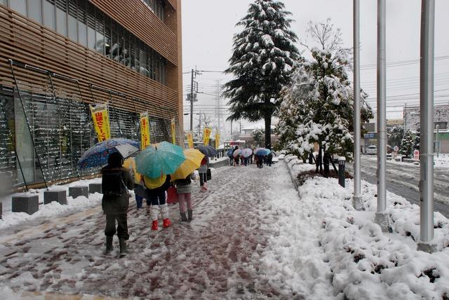 雪が積もる中、傘をさしながら登校する小学生の写真