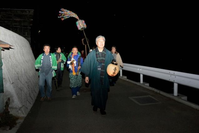夜道を緑の法被を着た保存会の男性たちが歩いている写真