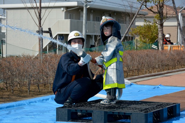 消防服を着て消防団員と共に放水を行う男の子の写真