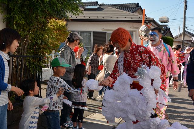 化粧コンテスト受賞者などの大行列が沿道で子供たちに花を渡す様子の写真