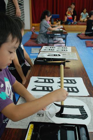 男の子が月という字を団扇に書いている写真