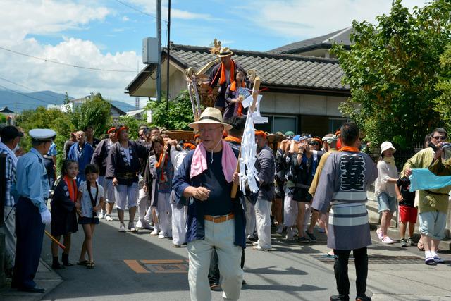 多くの人が神輿を担ぎ、先頭に帽子をかぶった男性が歩いている写真