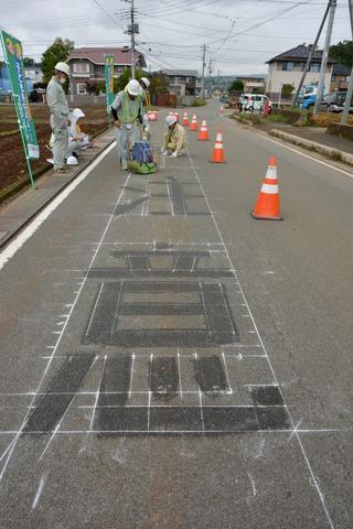 複数の作業員で地面に書かれた「注意」という字に「プライマー」と呼ばれる接着剤を塗っている写真