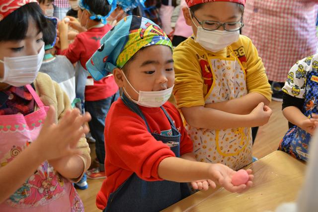 エプロンと三角巾をつけた園児たちが生地を丸くこねている写真