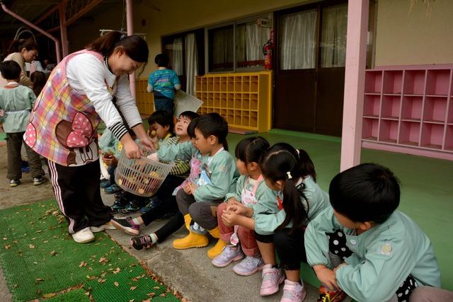 並んで座っている園児に先生からサツマイモが配られている様子の写真