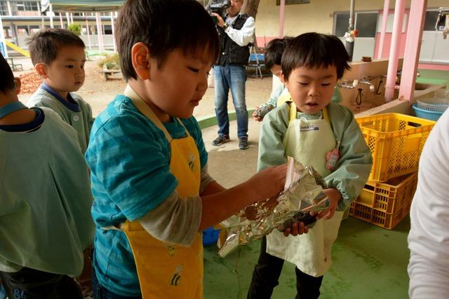 エプロン姿の園児たちがサツマイモを包むためのアルミホイルを手に取っている写真