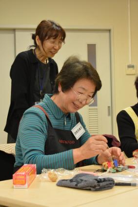 一人の女性が楽しそうに微笑みながら紙粘土で申を製作している写真