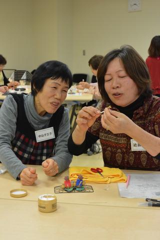 2人の女性が楽しそうに話しながら紙粘土で申を製作している写真